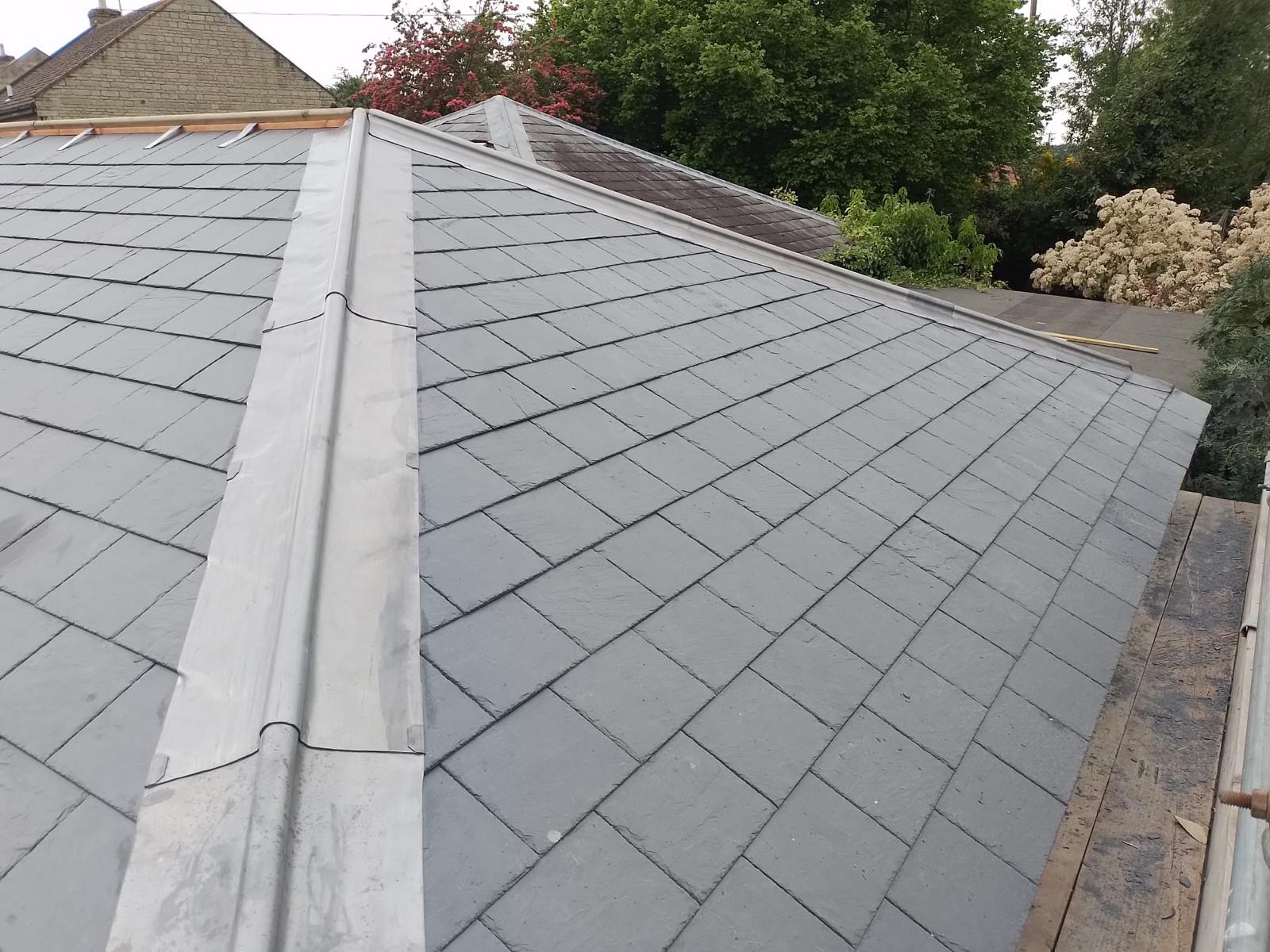 a neatly tiled slate roof with a metal ridge, surrounded by lush green trees and shrubs. the scene conveys a sense of newness and calm
