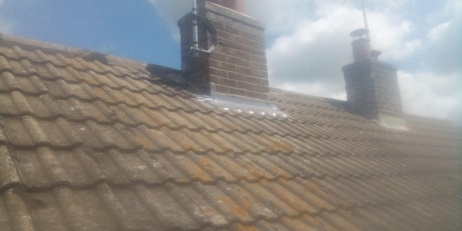 a slightly blurry image of a tiled roof with two brick chimneys under a cloudy blue sky. the roof appears weathered with patches of rust
