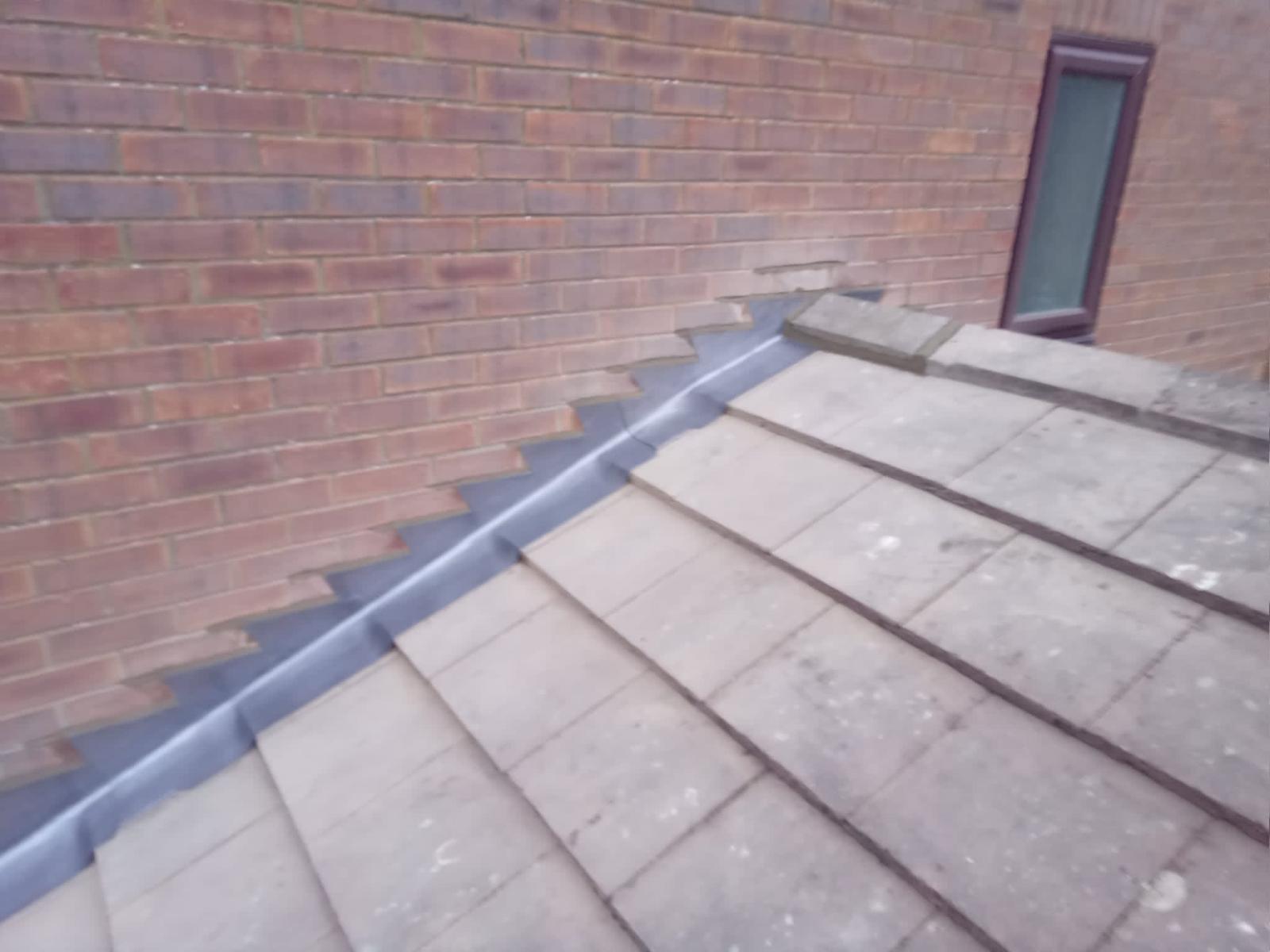 brick wall meeting a tiled roof with step flashing in between for waterproofing. the roof tiles are slightly weathered, and a small window is visible above