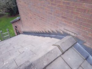 close up of a brick wall with stepped flashing over a sloped roof. the setting includes a ladder and grassy yard, conveying maintenance and structure