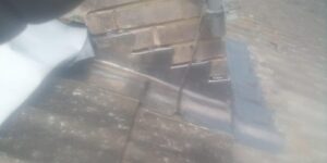 close up of shiny metal flashing on a sloped roof, meeting an old brick wall. the misty effect adds a muted, slightly mysterious tone
