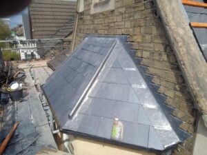 newly installed slate roof with a triangular shape on a historic building. a bottle of cleaner sits on the roof, with construction materials nearby.