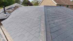 newly installed slate roof with clean lines and seamless symmetry. part of the neighboring house’s roof is visible, surrounded by trees under a clear sky