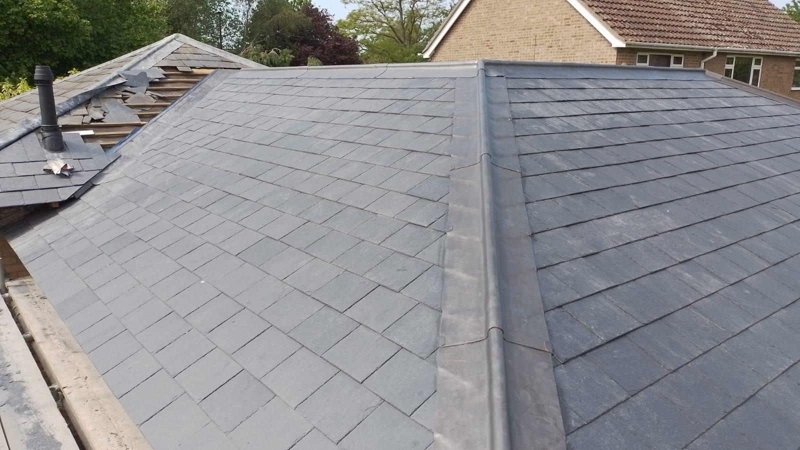 newly installed slate roof with clean lines and seamless symmetry. part of the neighboring house’s roof is visible, surrounded by trees under a clear sky