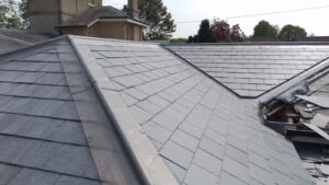 slate roof with neatly arranged tiles and metal flashing. surrounding trees and a chimney are visible, conveying a serene and tidy residential setting