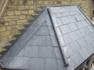 sloped slate roof with a neat lead flashing detail, adjacent to a brick wall. the roof has a clean, modern appearance with gray tones